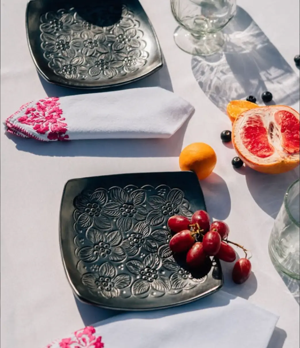 Embossed dark metal tableware with hand-embroidered linens