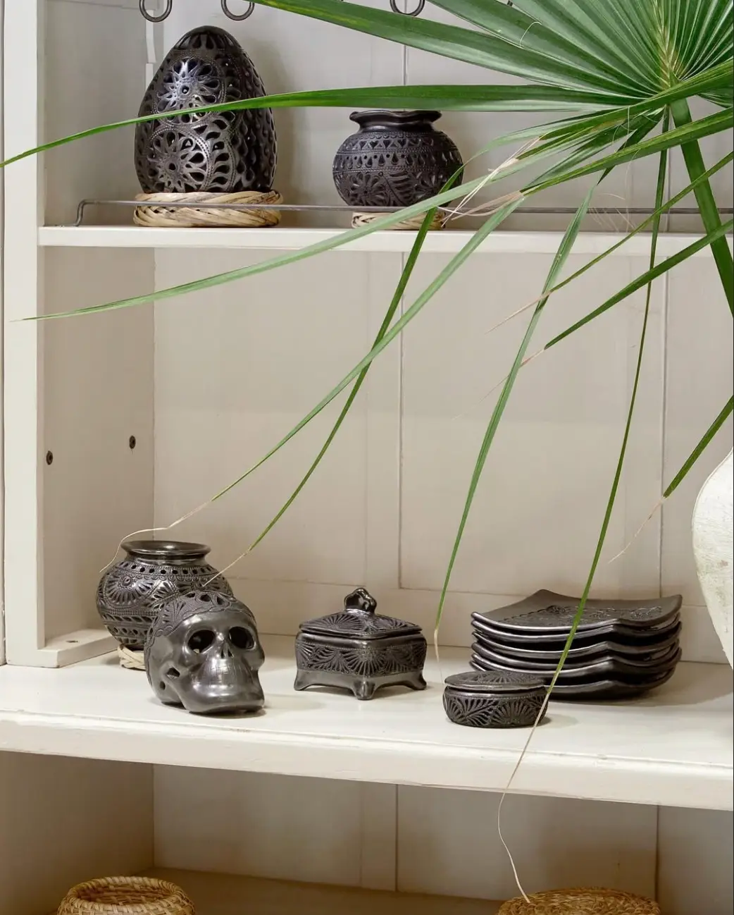 Hand-pierced black pottery displayed among palm leaves