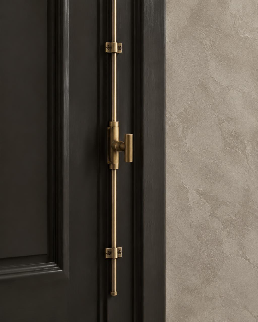 Bespoke antique brass cremone bolt on charcoal millwork beside hand-finished limestone plaster